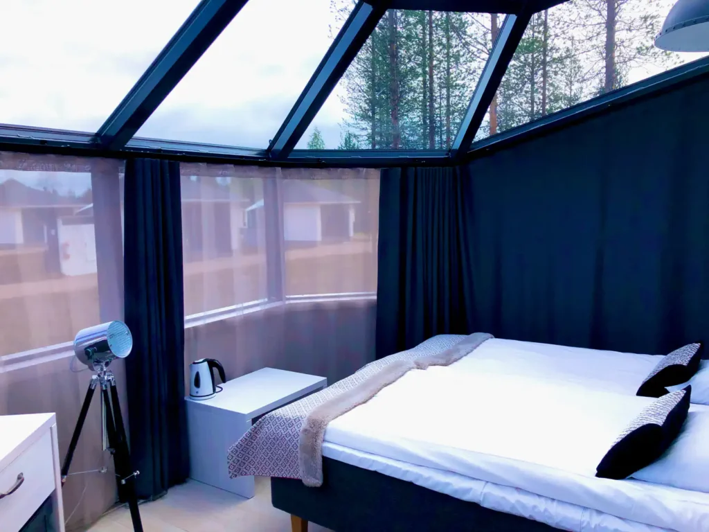 Interior view of a luxury glass igloo in Saariselkä, Finland, featuring a cozy bed under a transparent dome with views of the snowy forest.