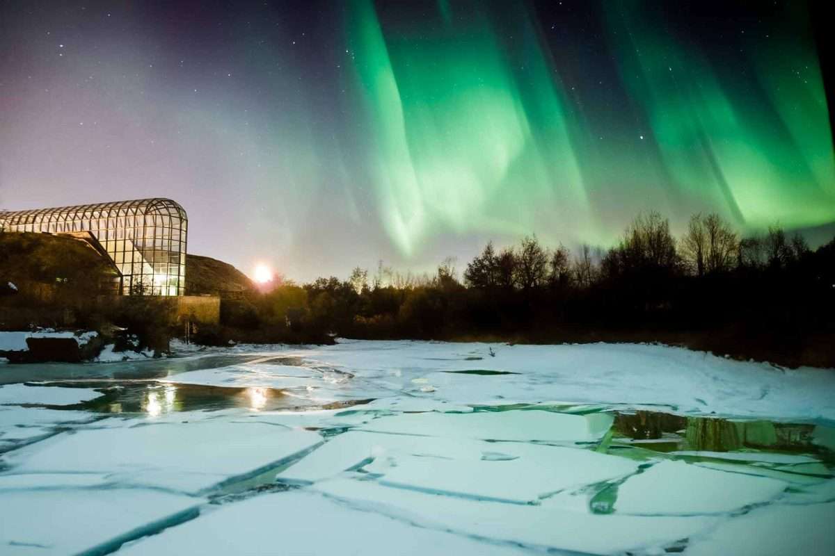 Arktikum Museum in Rovaniemi, Finland, under the Northern Lights with a partially frozen river and icy foreground.