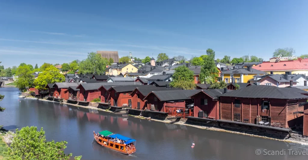 Iconic red shorehouses along the Porvoo River with a sightseeing boat in Finland
