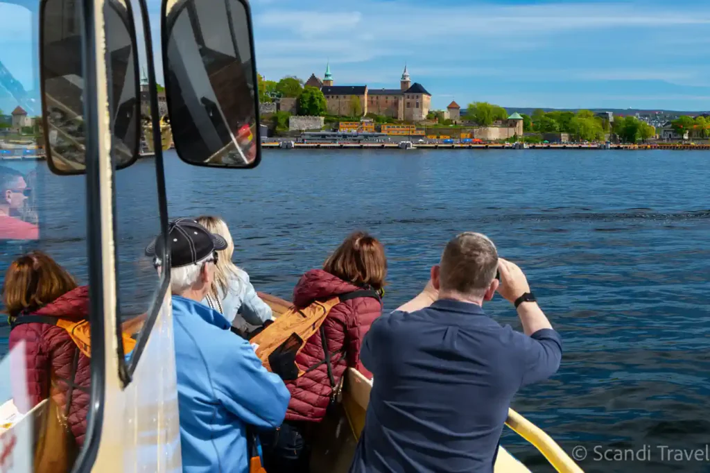 Tourists on Scandi Travel boat tour in Oslo viewing Akershus Fortress across the Oslofjord