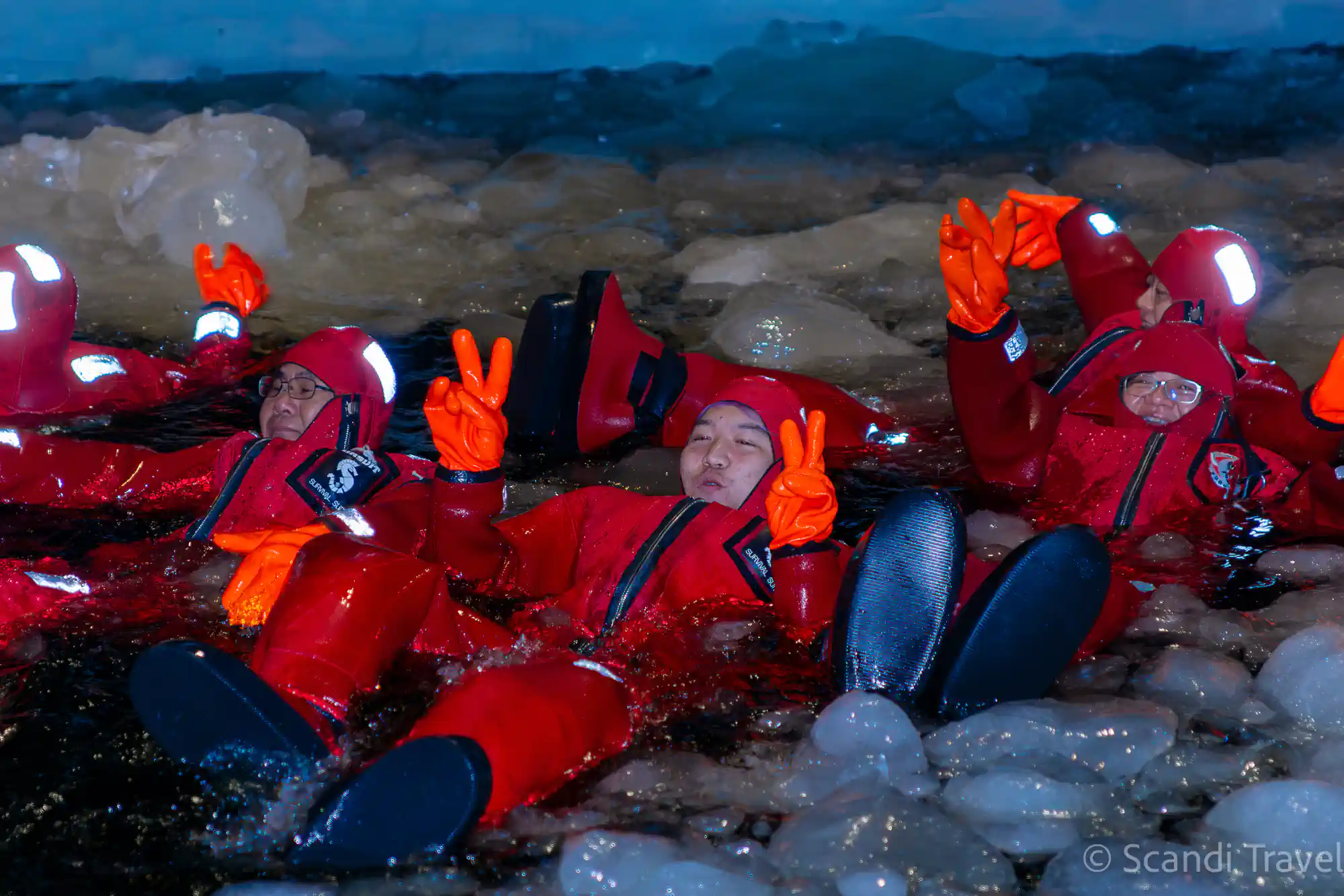 Group of travellers in red survival suits floating among the ice in the Gulf of Bothnia during the Sampo icebreaker cruise, 7-day Lapland Northern Lights tour