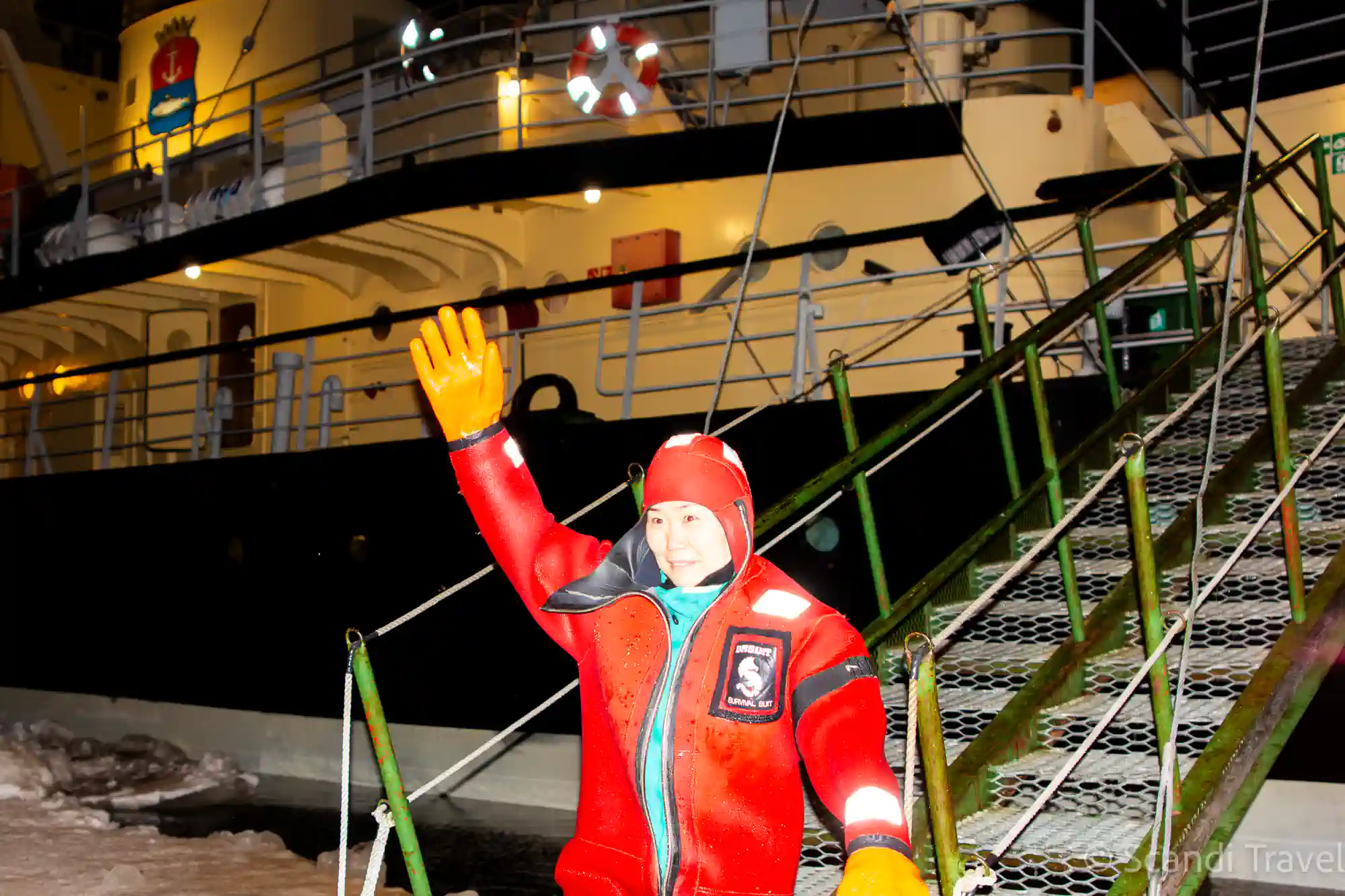 Traveller in a red survival suit waving after the ice swim beside the Sampo icebreaker in Kemi, on the 7-day Lapland Northern Lights tour
