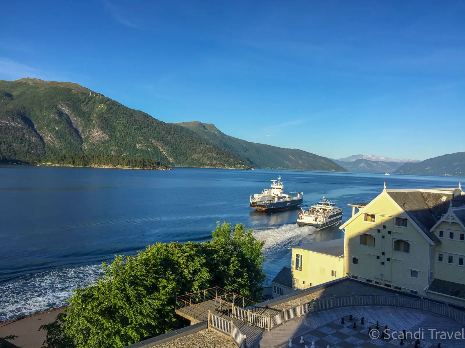 Passenger ferries crossing the Sognefjord near the historic yellow hotel in Balestrand, Norway.