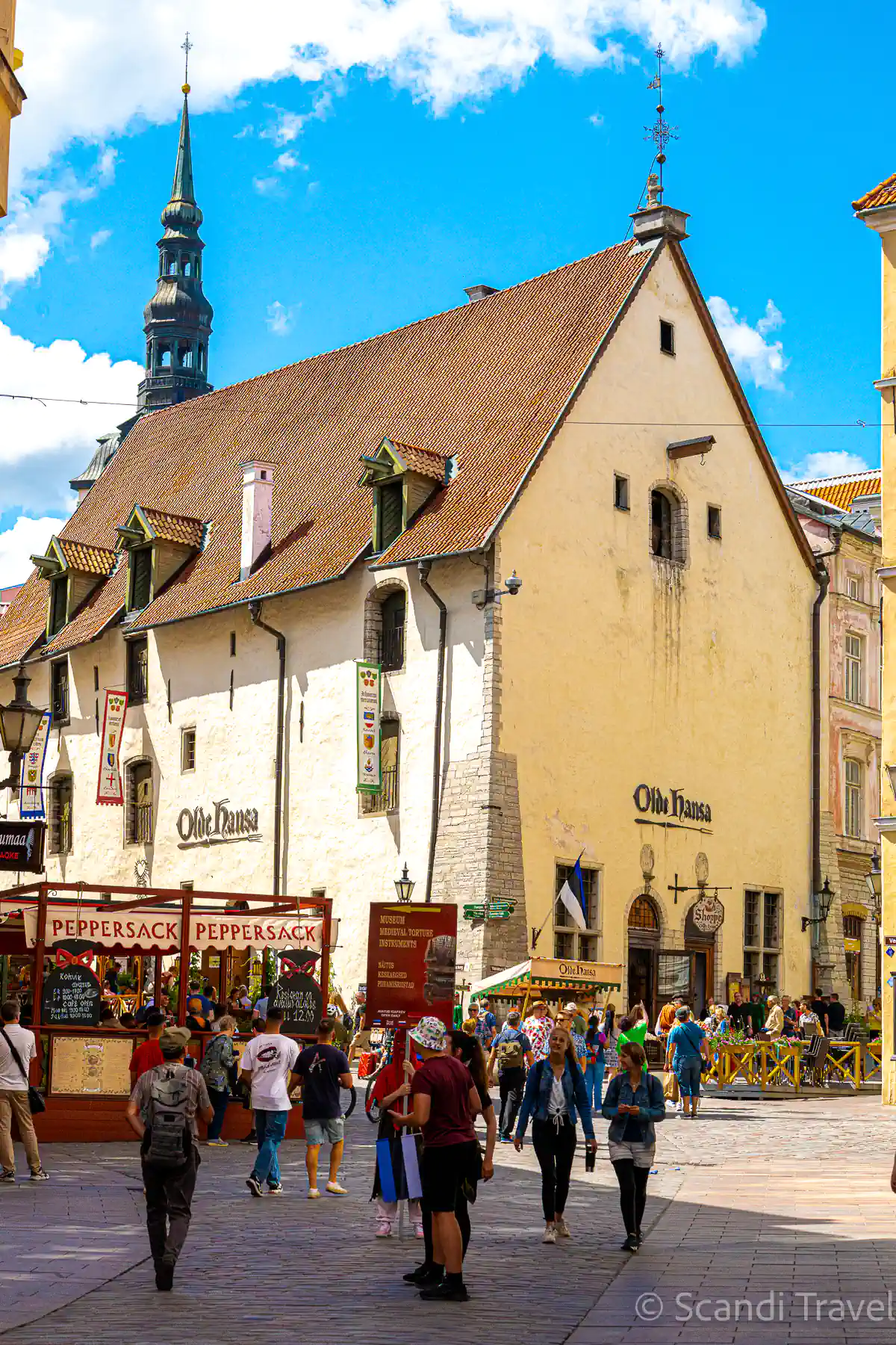 Medieval merchant house of the Olde Hansa restaurant in Tallinn Old Town, with the Town Hall spire behind and visitors on the cobbled street