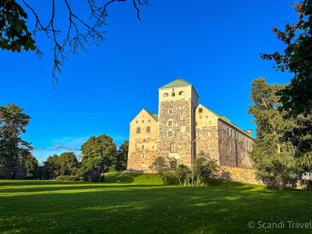 Medieval Turku Castle in warm evening light, with green lawns and trees under a deep blue summer sky