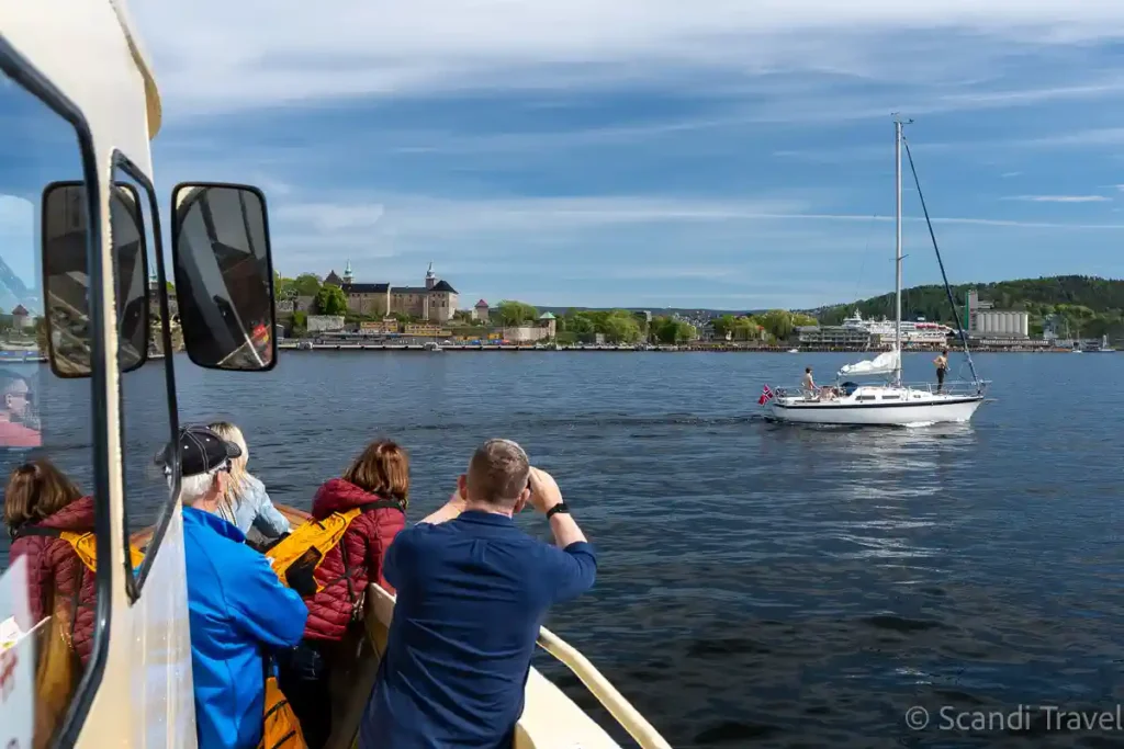 Guests on an Oslofjord sightseeing cruise photographing a sailboat and Akershus Fortress on Day 4 of Scandi Travel’s 10-day tour
