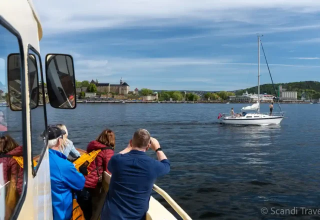 Guests on an Oslofjord sightseeing cruise photographing a sailboat and Akershus Fortress on Day 4 of Scandi Travel’s 10-day tour
