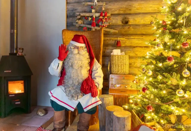 Santa Claus greeting visitors inside a cozy wooden cabin at Santa Claus Village in Lapland during Arctic Adventure tour