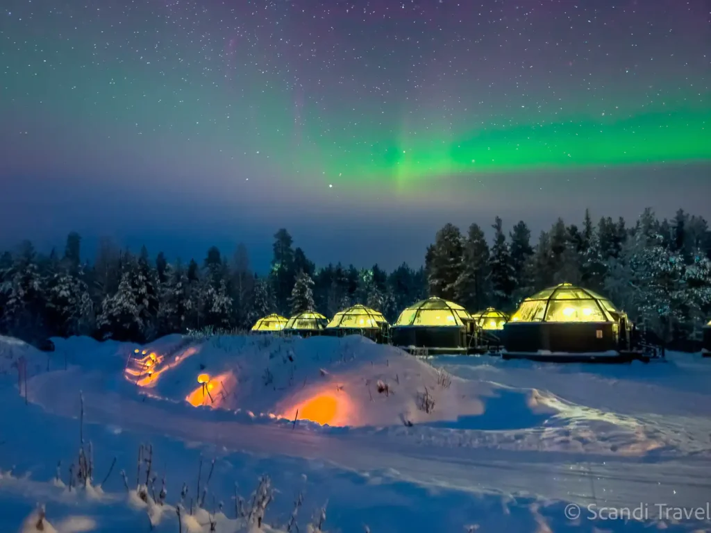 Glass igloo in Finnish Lapland glowing under green Northern Lights on a winter night
